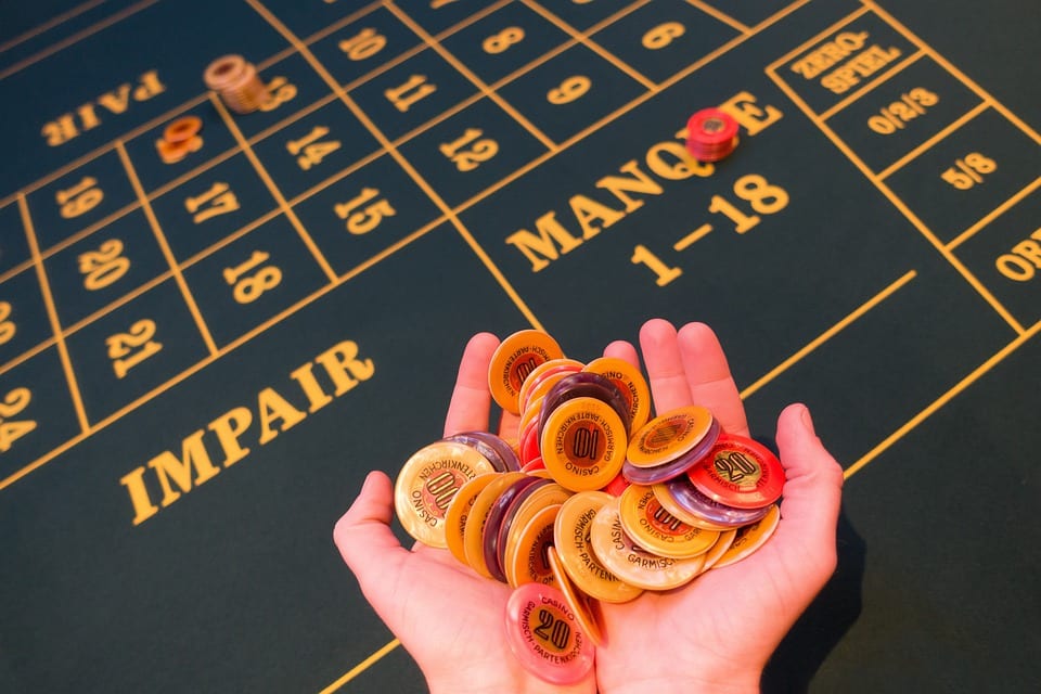 des mains pleine de jetons de casino au dessus d'une table de roulette